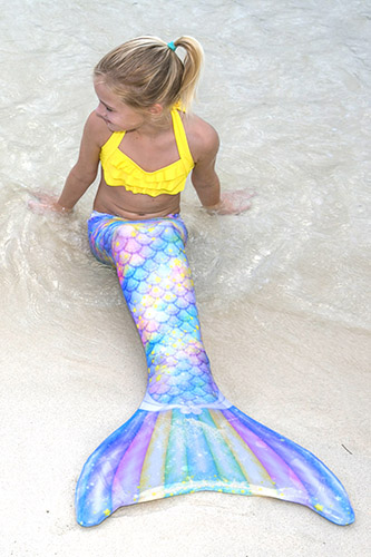 a young mermaid sits in the sand wearing the sweet dreams limited edition mermaid tail