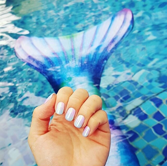 someone holding up their mermaid nails that match their mermaid tail by the pool