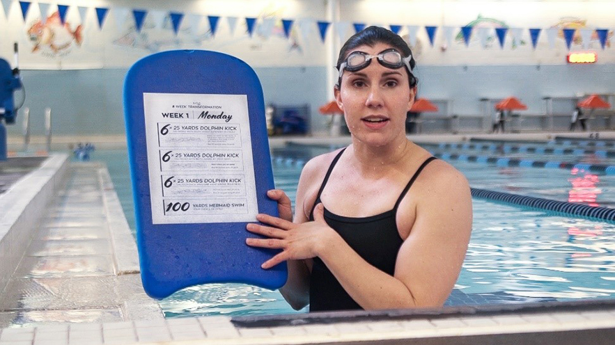 a swim coach wearing goggles in a pool and holding up a paper with the day's workout 