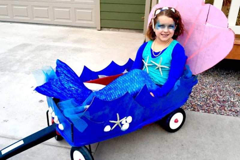 a young girl in the Arctic Blue mermaid tail riding in a sea-themed wagon