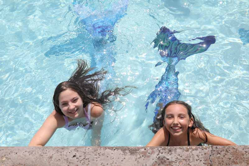 two happy girls swimming in mermaid tails