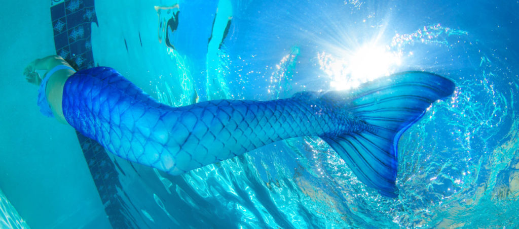 A girl swimming in a pool with the Blue Lagoon mermaid tail.