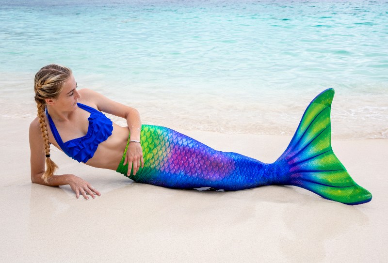 A girl in a swimmable mermaid tail that is yellow, green, blue, and purple.