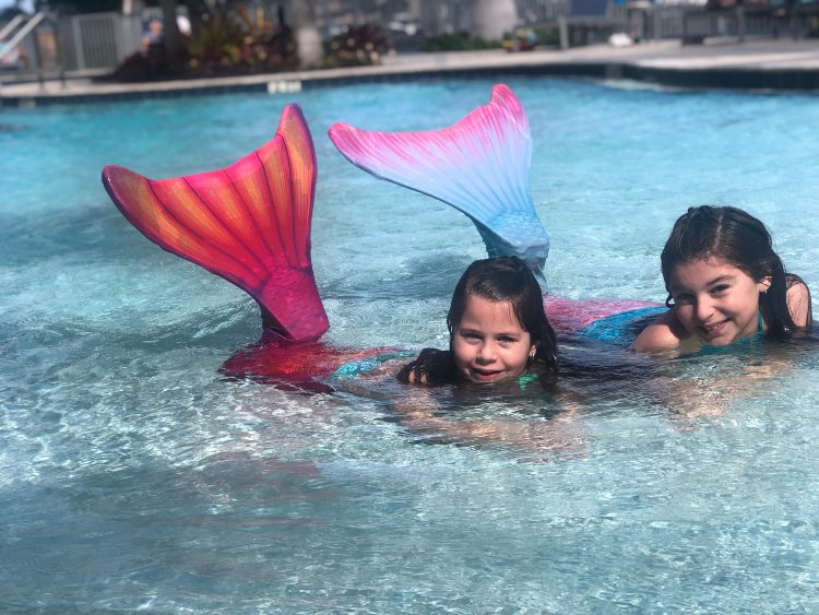 two girls posing in their swimmable mermaid tails in a pool