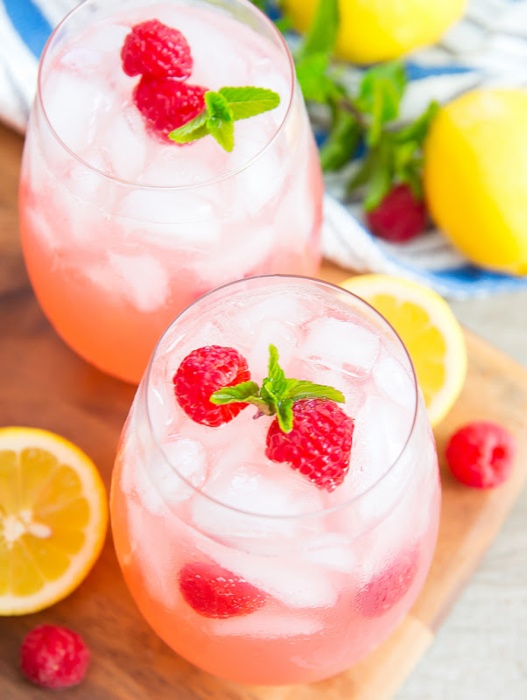 sparkling pink lemonade drink in two glasses with fresh raspberry and mint garnish