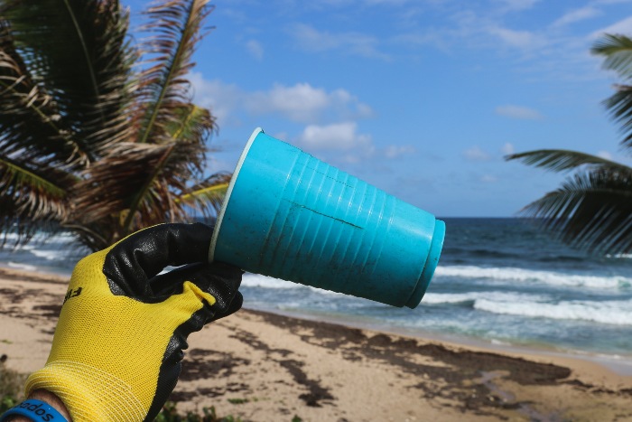 person holding up a plastic cup that was found on the beach