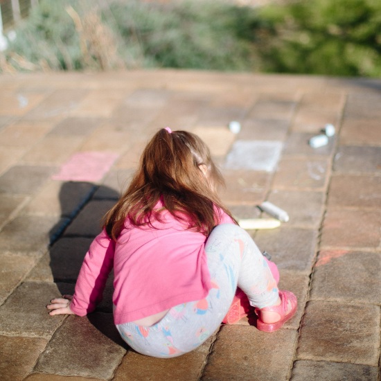 a girl outside drawing with sidewalk chalk