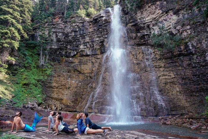 a merman leading a group in yoga in front of a waterfall