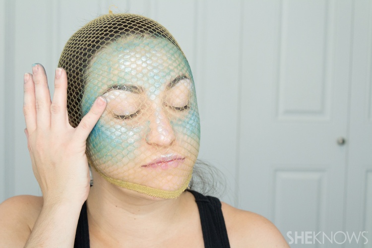 woman applying highlighter while wearing fishnets on her face