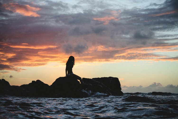 mermaid silhouette sitting on rocks in the ocean