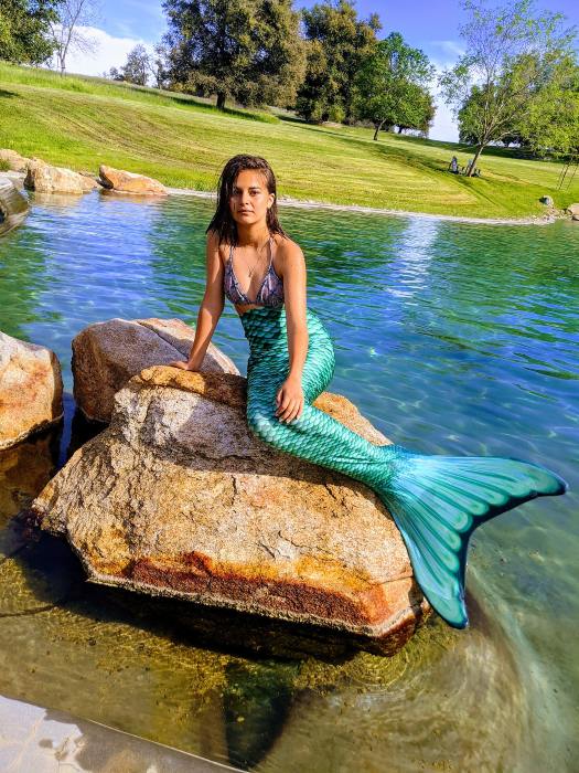 girl wearing the Celtic Green Mermaidens tail poses on a rock in a pond
