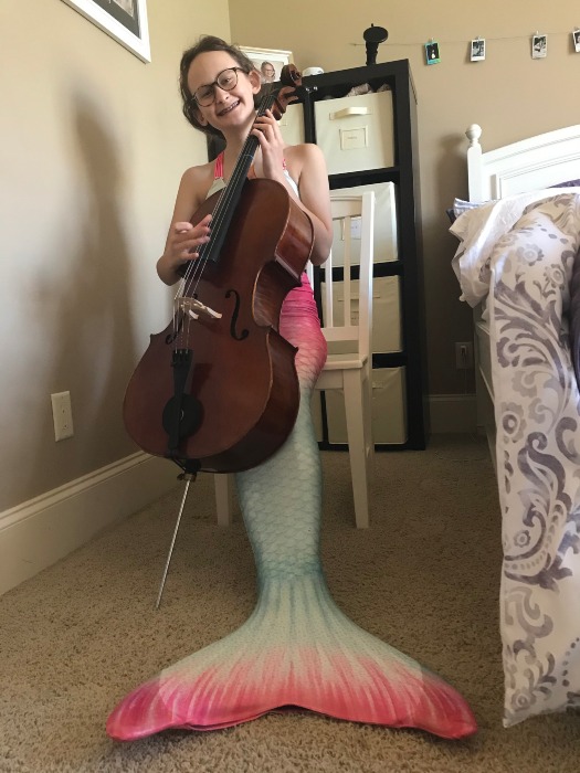 girl in a mermaid tail sitting on a chair and playing the cello