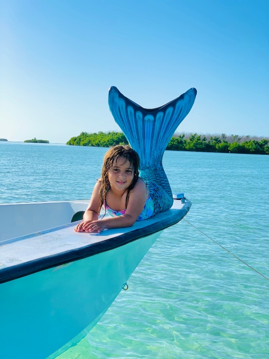 little girl in a teal mermaid tail poses on the side of a boat