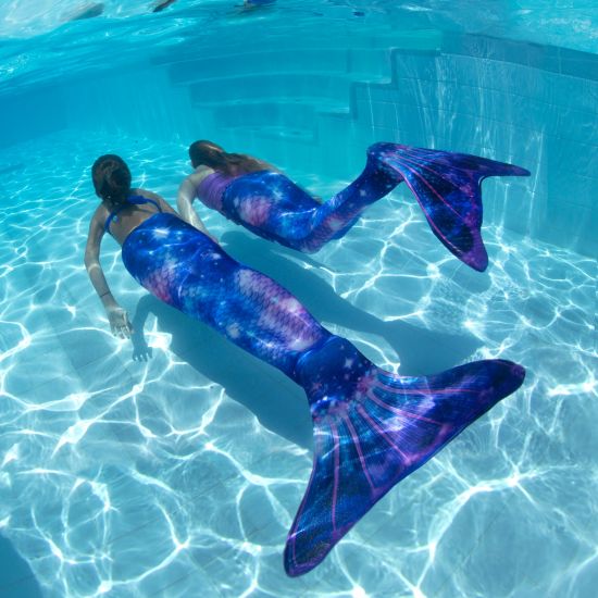 two girls swimming underwater in purple galaxy mermaid tails