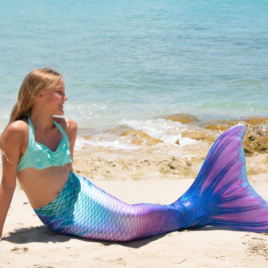 girl wearing a purple and mint mermaid tail in front of the ocean