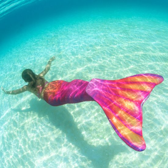 girl swimming underwater in a bright pink and orange mermaid tail