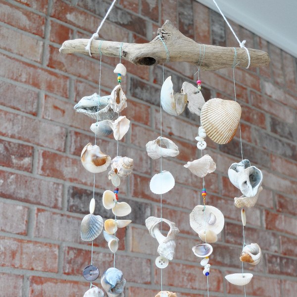 a wind chime made with driftwood, sea shells, buttons, and beads hanging in front of a brick wall