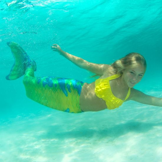 girl swimming on her side underwater in a yellow, green, and blue mermaid tail