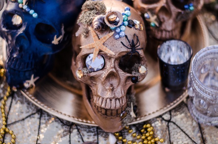 gold and blue decorative skulls covered in starfish, shells, spiders, moss, and gems