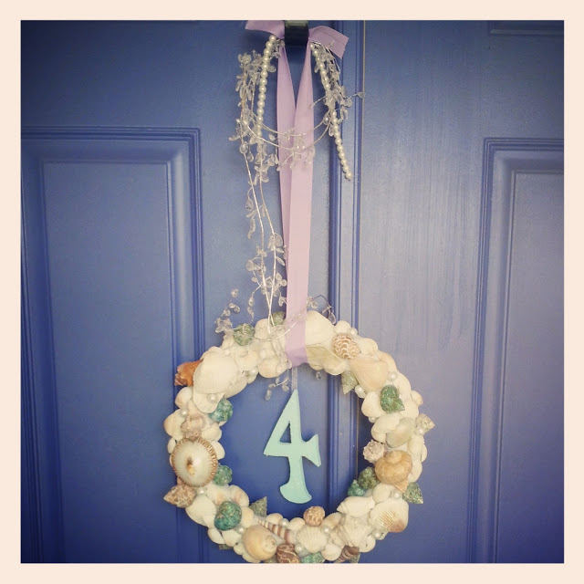 a mermaid wreath covered in seashells hanging on a blue door