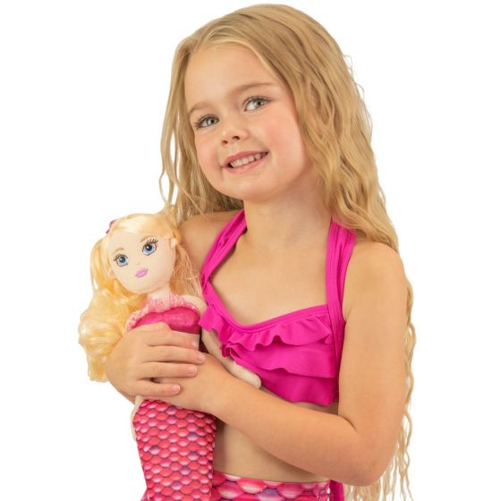 A young girl holds the Waverlee Mermaidens doll wearing matching pink scales.