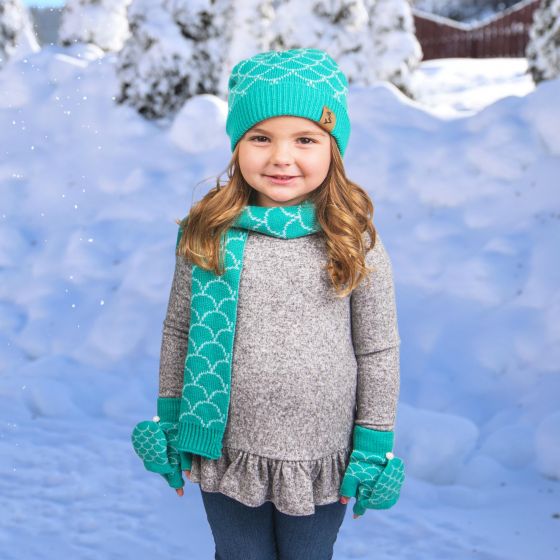 A girl wearing the hat, mitten, and scarf set stands in front of a snowy background.