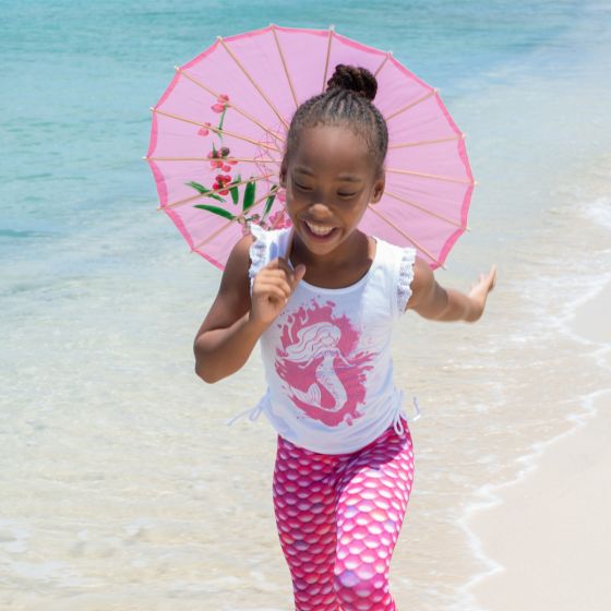 A girl runs on the beach wearing a mermaid tank top and pink scale leggings.