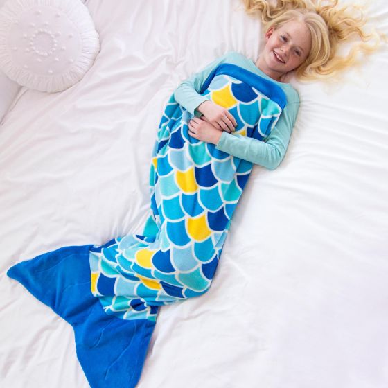 A girl lays on a bed in a blue mermaid tail blanket.