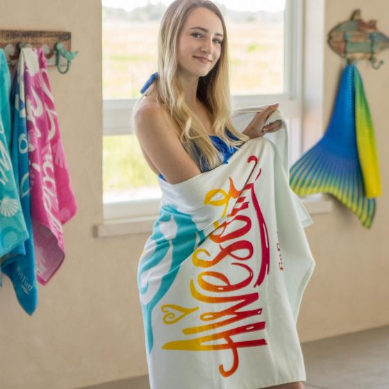 A girl wrapped in a mermaid beach towel stands by the pool.