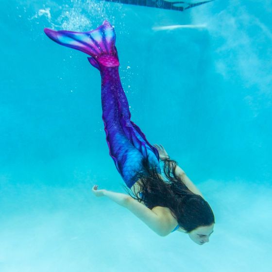 a girls dives underwater in a blue and pink mermaid tail that has side, ankle, and dorsal fins