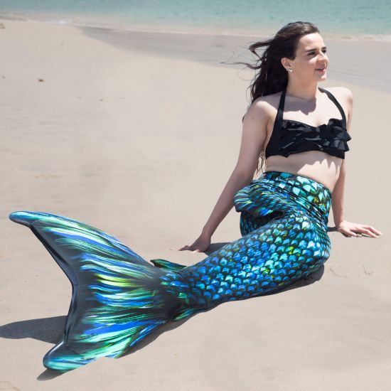 a girls lays on the beach wearing a blue and green mermaid tail with side fins