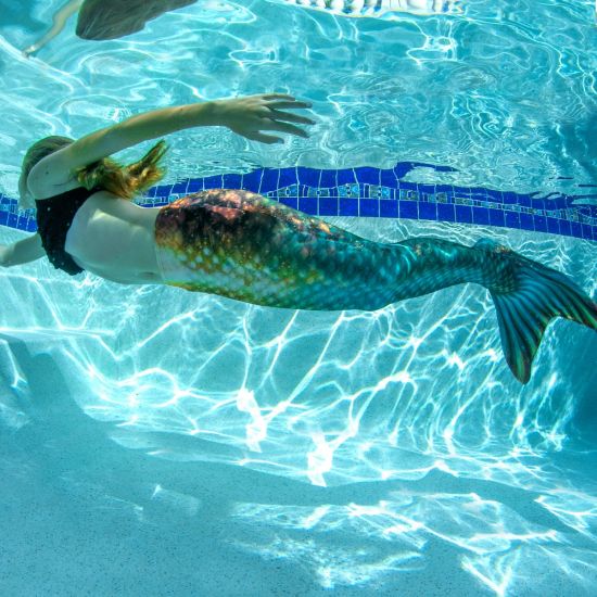 a girl swimming underwater in a green and bronze mermaid tail