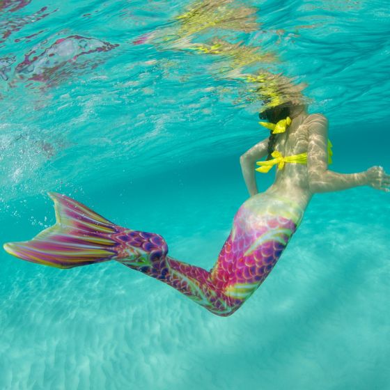 an underwater shot of a mermaid swimming underwater in a pink and gold mermaid tail