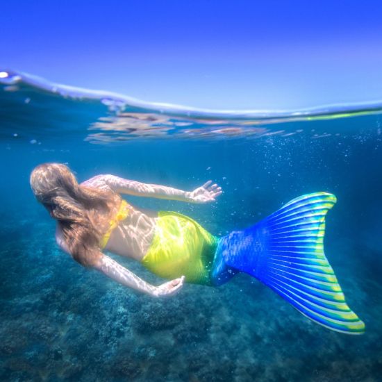 an underwater shot of a mermaid swimming in a yellow and blue mermaid tail