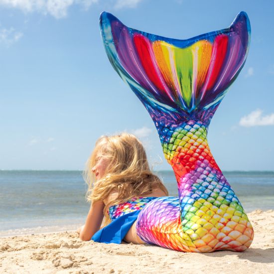 a mermaid laying on the beach in a rainbow mermaid tail